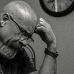 Grayscale Photo of Man Thinking in Front of Analog Wall Clock